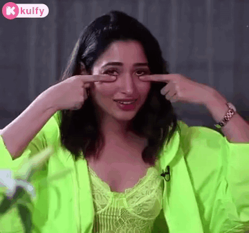 A Woman In A Neon Green Jacket Is Pointing At Her Eye . GIF