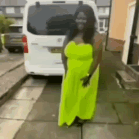 A Woman In A Neon Yellow Dress Is Standing In Front Of A White Van On A Sidewalk . GIF