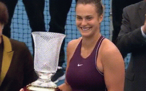 A Woman In A Nike Tank Top Is Holding A Trophy GIF