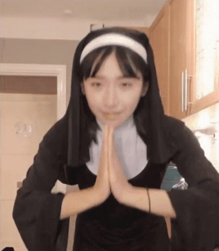 A Woman In A Nun Costume Is Praying With Her Hands Together . GIF