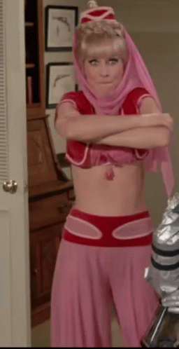 A Woman In A Pink And Red Costume With Her Arms Crossed Is Standing In A Room . GIF