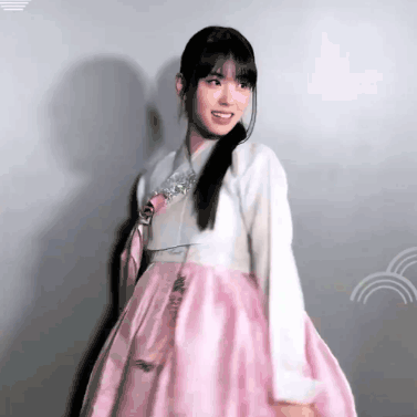 A Woman In A Pink And White Dress Is Standing In Front Of A Wall And Smiling . GIF