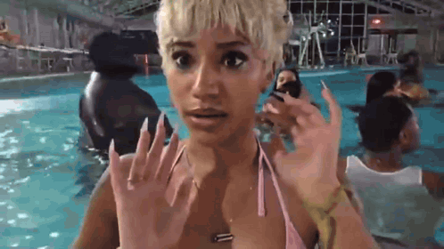 A Woman In A Pink Bikini Is Standing In A Swimming Pool With A Surprised Look On Her Face . GIF