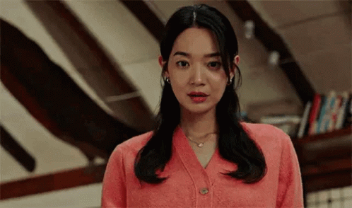 A Woman In A Pink Cardigan Is Standing In A Room . GIF