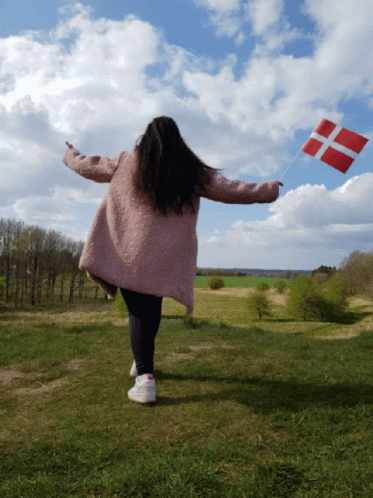 A Woman In A Pink Coat Holds A Red And White Flag In A Field GIF