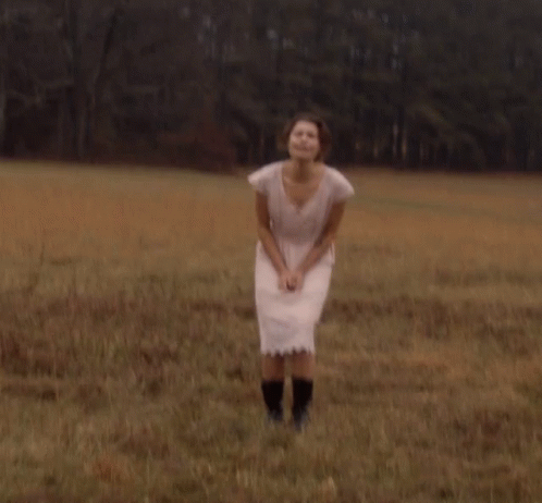 a woman in a pink dress and black boots stands in a field