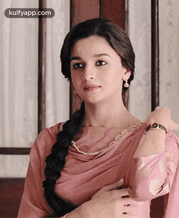 A Woman In A Pink Dress And Braided Hair Is Looking At The Camera . GIF