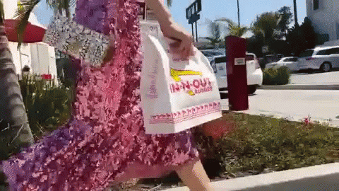 A Woman In A Pink Dress Is Carrying A Bag That Says In-N-Out GIF