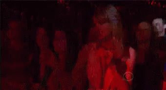 A Woman In A Pink Dress Is Dancing In A Crowd Of People . GIF