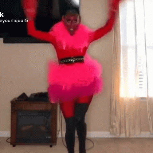 A Woman In A Pink Dress Is Dancing In Front Of A Fireplace . GIF