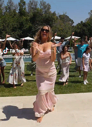 A Woman In A Pink Dress Is Dancing In Front Of A Group Of People With A Tik Tok Watermark GIF