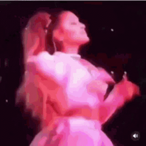 A Woman In A Pink Dress Is Dancing On A Stage While Holding A Microphone . GIF