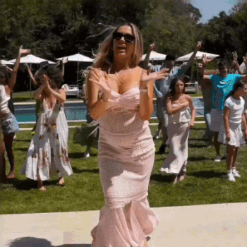 A Woman In A Pink Dress Is Dancing With A Group Of People In A Backyard . GIF
