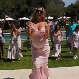 A Woman In A Pink Dress Is Dancing With A Group Of People In Front Of A Swimming Pool . GIF