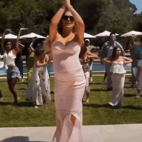 A Woman In A Pink Dress Is Dancing With A Group Of People . GIF