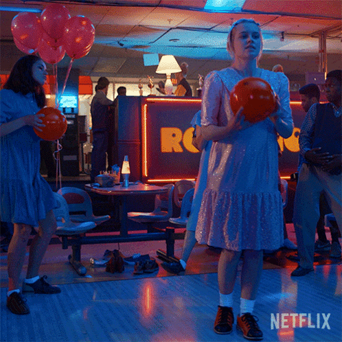 A Woman In A Pink Dress Is Holding A Bowling Ball In A Bowling Alley With Netflix Written On The Bottom GIF