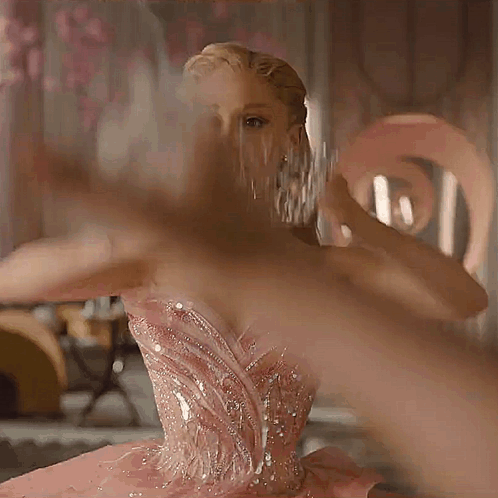A Woman In A Pink Dress Is Holding A Crown On Her Head GIF