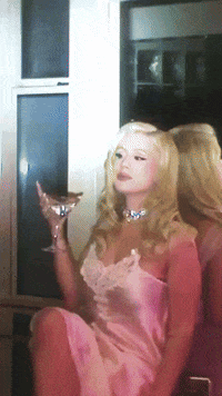 A Woman In A Pink Dress Is Holding A Glass Of Champagne GIF