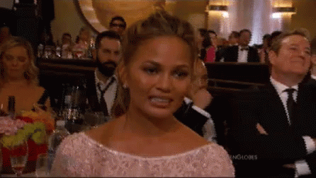 A Woman In A Pink Dress Is Making A Funny Face While Sitting In A Crowd Of People . GIF
