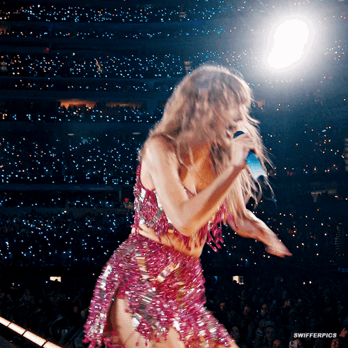 A Woman In A Pink Dress Is Singing Into A Microphone On A Stage GIF