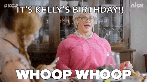 A Woman In A Pink Dress Is Sitting At A Table With A Woman In A Wig And Glasses . GIF