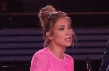 A Woman In A Pink Dress Is Sitting In Front Of A Microphone And Making A Face . GIF