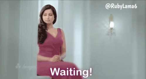 A Woman In A Pink Dress Is Sitting In Front Of A Wall That Says Waiting GIF