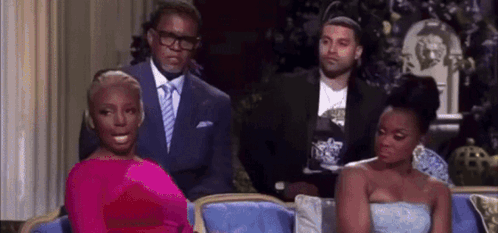 A Woman In A Pink Dress Is Sitting On A Couch Next To Two Men In Suits . GIF