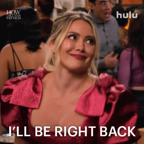 A Woman In A Pink Dress Is Smiling And Says I 'Ll Be Right Back GIF