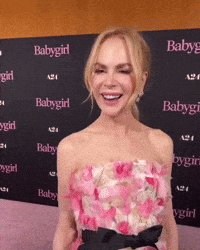 A Woman In A Pink Dress Is Smiling In Front Of A Wall With Babygirl Written On It GIF