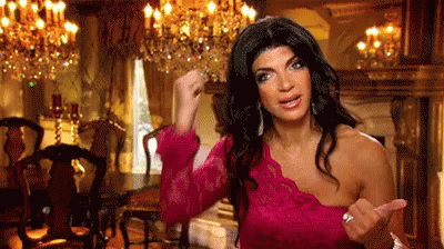 A Woman In A Pink Dress Is Standing In A Dining Room With A Fist In The Air . GIF