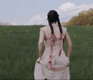 A Woman In A Pink Dress Is Standing In A Grassy Field With Her Hands In Her Pockets . GIF