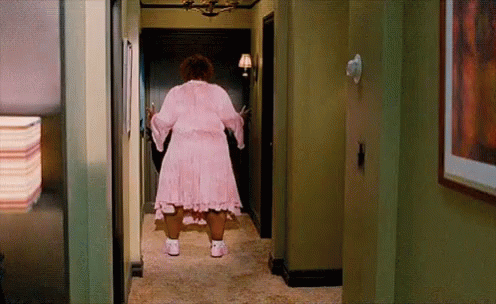 A Woman In A Pink Dress Is Standing In A Hallway . GIF