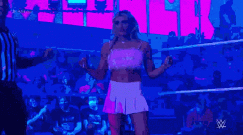 A Woman In A Pink Dress Is Standing In A Wrestling Ring With A Referee GIF