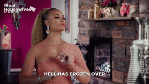 A Woman In A Pink Dress Is Standing In Front Of A Fireplace And Says " Hell Has Frozen Over " GIF