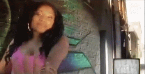 A Woman In A Pink Dress Is Standing In Front Of A Wall With Graffiti On It . GIF