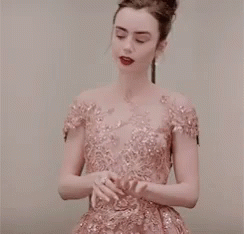 A Woman In A Pink Dress Is Standing In Front Of A White Wall . GIF