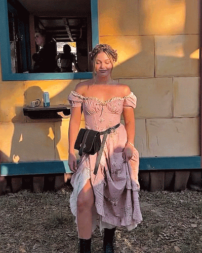 A Woman In A Pink Dress Is Standing In Front Of A Yellow Building GIF
