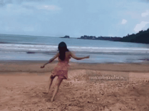 A Woman In A Pink Dress Is Walking On A Beach With The Name Mambazalien On The Sand GIF