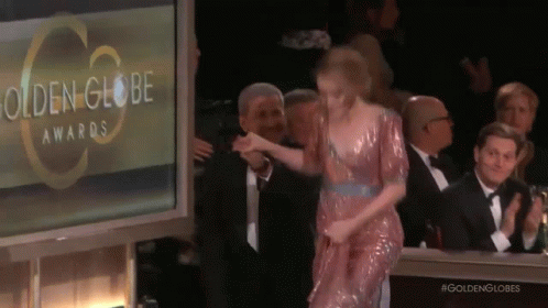 A Woman In A Pink Dress Is Walking On A Stage At The Golden Globe Awards GIF