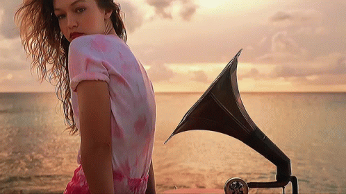 A Woman In A Pink Dress Stands In Front Of A Gramophone GIF
