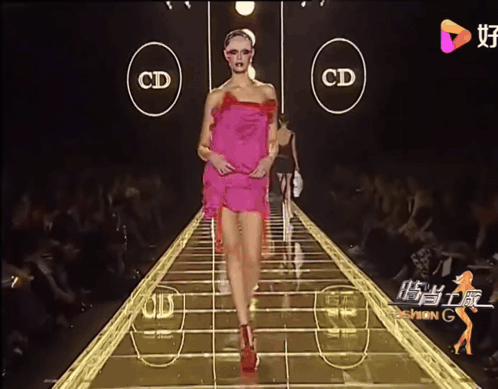 A Woman In A Pink Dress Walks Down A Runway With The Letters Cd On The Side GIF