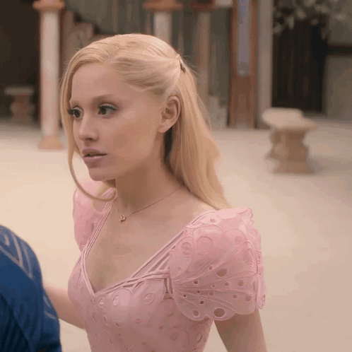 A Woman In A Pink Dress With Butterfly Sleeves Looks To The Side GIF