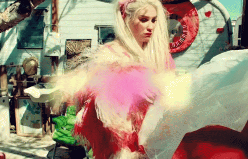 A Woman In A Pink Dress With Feathers Is Standing In Front Of A Trailer GIF