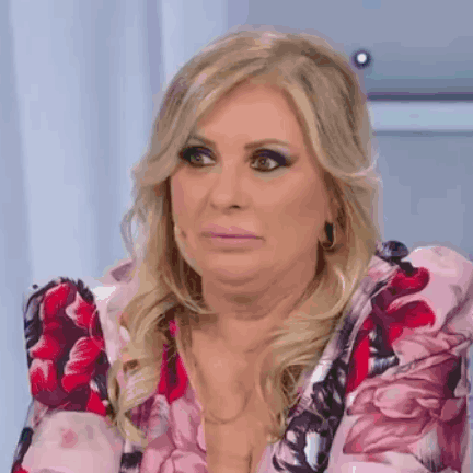 A Woman In A Pink Floral Dress Is Making A Funny Face While Sitting On A Chair . GIF