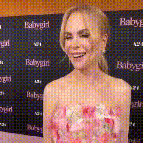 A Woman In A Pink Floral Dress Is Smiling In Front Of A Baby Girl Sign . GIF