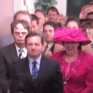 A Woman In A Pink Hat Is Standing In Front Of A Crowd Of People In Suits And Ties . GIF
