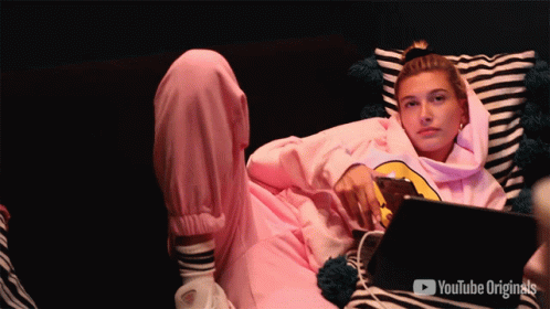 A Woman In A Pink Hoodie Is Laying On A Couch With A Youtube Originals Logo Behind Her GIF