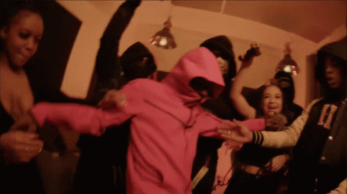 A Woman In A Pink Hoodie Is Surrounded By A Crowd Of People GIF