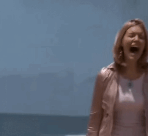 A Woman In A Pink Jacket And A White Skirt Is Standing On A Beach . GIF